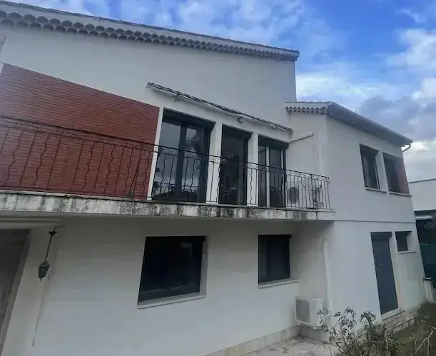 renovation totale de menuiseries alu charleval Façade maison moderne avec balcon, ciel nuageux.